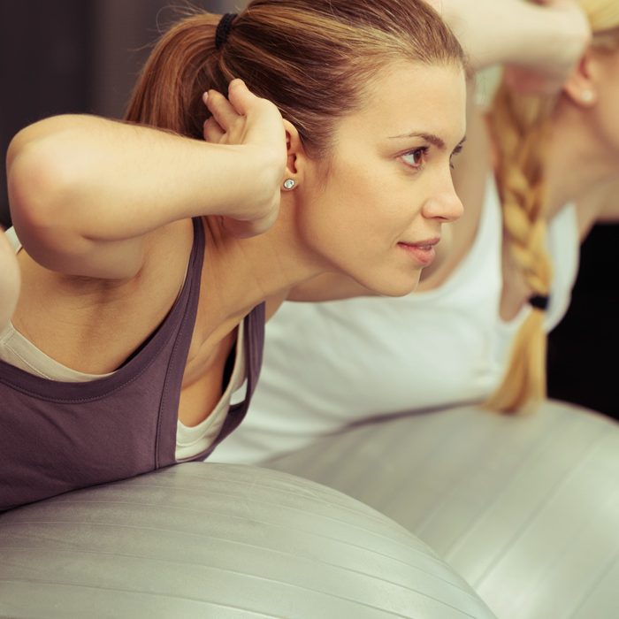 Eine Frau in Sportkleigung liegt bäuchlings auf einem Gymnasikball und fixiert ihre Hände neben dem Kopf seitlich